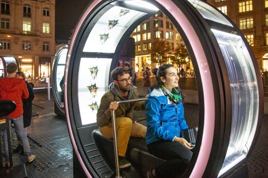 Zwei Personen sitzen abends in einem Loop auf dem Rathenauplatz