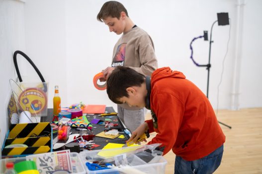 Foto von zwei jugendlichen Workshopteilnehmern an einem bunten Basteltisch.